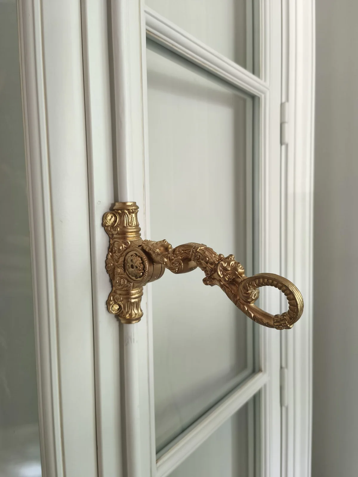 Crémone ancienne en laiton rénovée et reposée sur une fenêtre blanche
